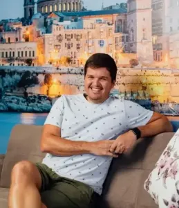 A man wearing a white shirt and green shorts sitting on a couch.