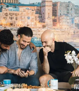 A group of people having a conversation together. The person in the middle is holding their mobile phone.