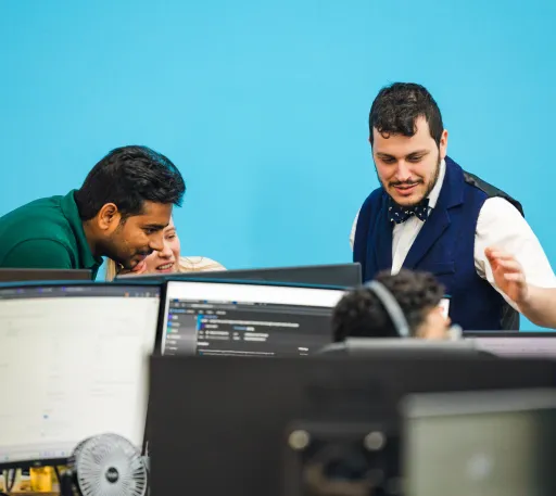 Three colleagues collaborating at their desks in an office with a vibrant blue wall, focusing on computer screens.