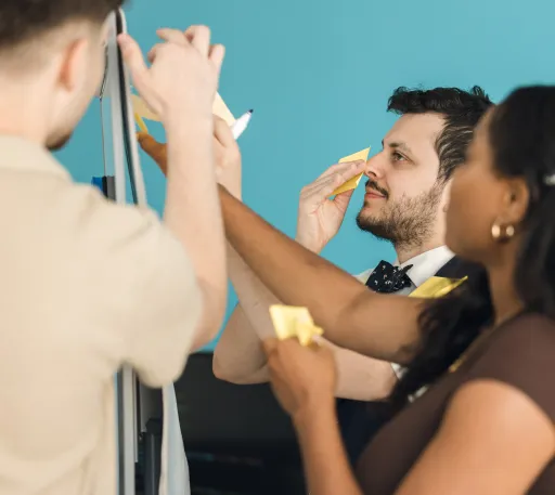 A software team working, looking up at a whiteboard with post it notes in hand.
