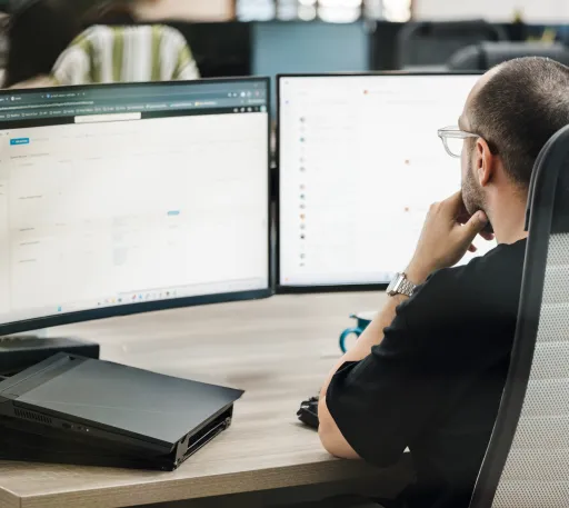 An IT operations manager working, looking at two computer monitors.