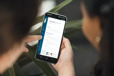 A person holds a smartphone, pointing to a digital résumé being displayed.