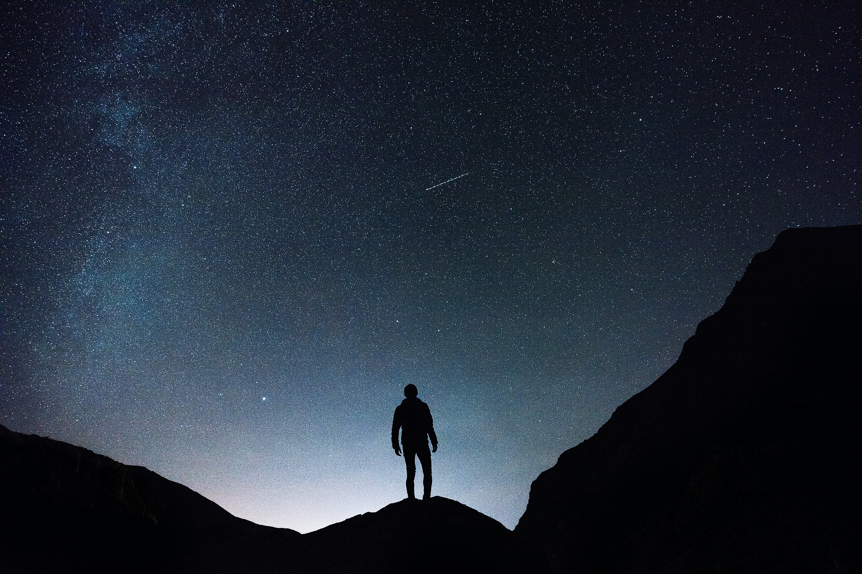 Silhouette of a person standing on a mountain under a starry night sky